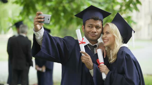 Young People in Graduation Outfit Taking Selfie with Mobile Phone, Looking at It