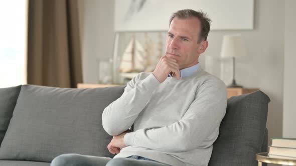 Serious Middle Aged Businessman Sitting on Sofa and Thinking