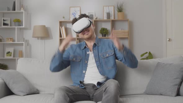 Young Caucasian Man Wearing Virtual Reality Glasses at Home in the Living Room