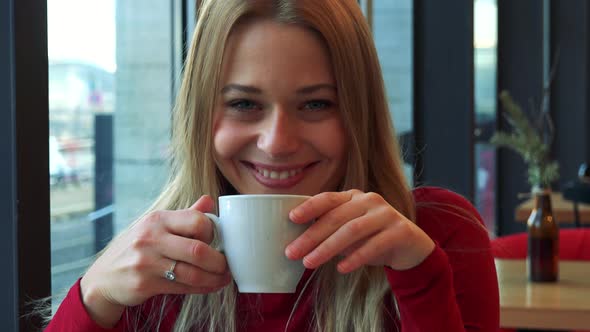 A Young Attractive Woman Sits at a Table in a Cafe, Drinks Tea and Smiles at the Camera - Closeup