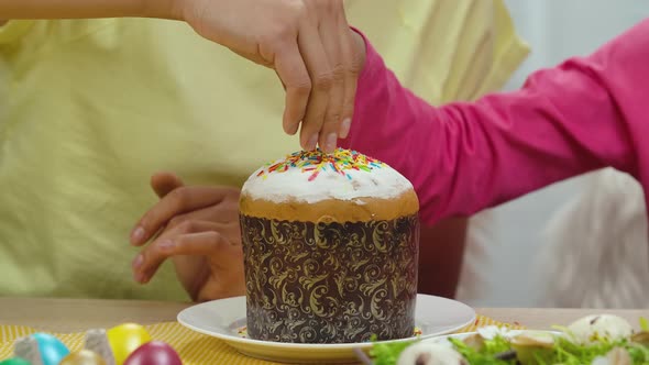 Mom and Daughter with Funny Bunny Ears Decorate Easter Cake with Sweet Candies