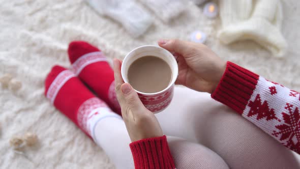 Woman Hands Holding a Cup of Hot Cocoa on the Background of a Garland in the Christmas Decorations