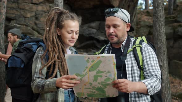 Group of People Tourists Looking at Map and Discussing Trip Standing in Forest Together