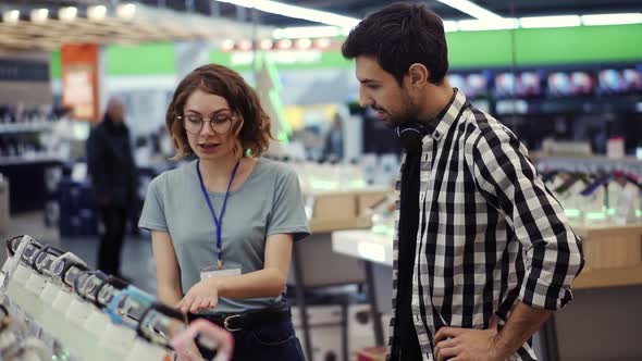 In the Electronics Store Female Consultant Gives Professional Advice to a Young Man