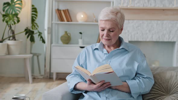 Relaxed Old Woman Reading Paper Book Novel Bestseller Sitting on Sofa Spending Cozy Weekend at Home