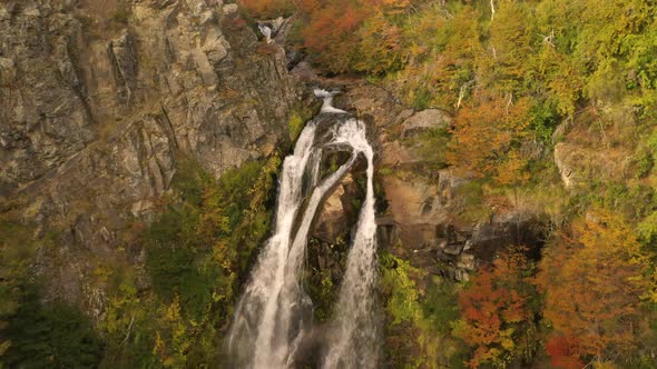 Cinematic aerial shot of a waterfall and revealing an autumnal woodland in Patagonia, Argentina