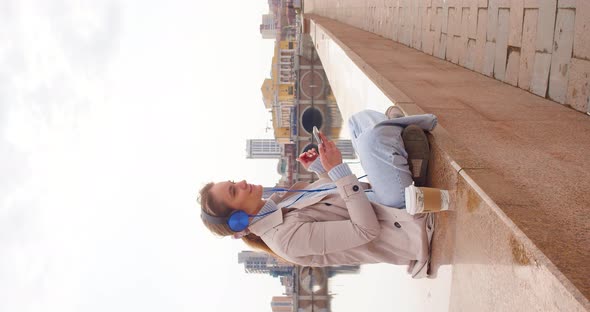 A Young Woman in Headphones and Listens to Relaxing Music on the Embankment She Having Rest From