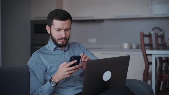 Man Using Smartphone and Laptop at Home