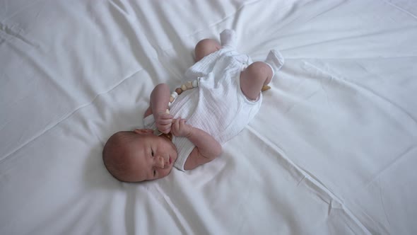 Wide Shot Caucasian Newborn Boy Lying on White Bed Indoors Looking Away