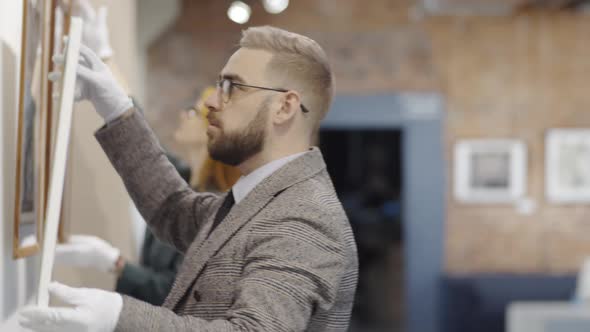 Male Worker Placing Painting on Wall in Art Gallery