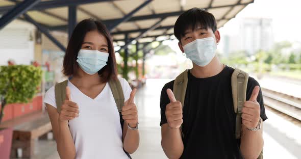 Couple show thumbs up look at camera stand in train station