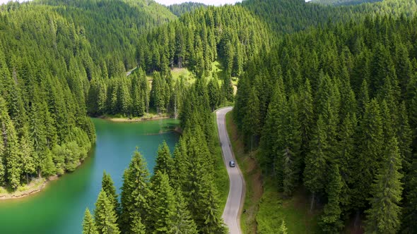 Aerial view of car driving through the fores and the lake on the side, Beautiful mountain road