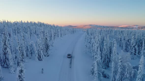 Aerial view above vehicle travelling freezing snowy remote woodland road towards sunrise mountain la