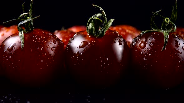 Cherry tomatoes on a black background in water drops.