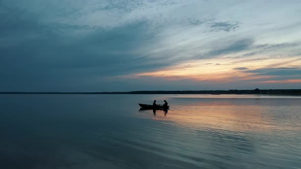 Silhouettes of Two Fishermen Sailing on a Small Boat at Sunset