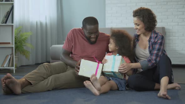 Cute little girl receiving presents from parents for her birthday in living room