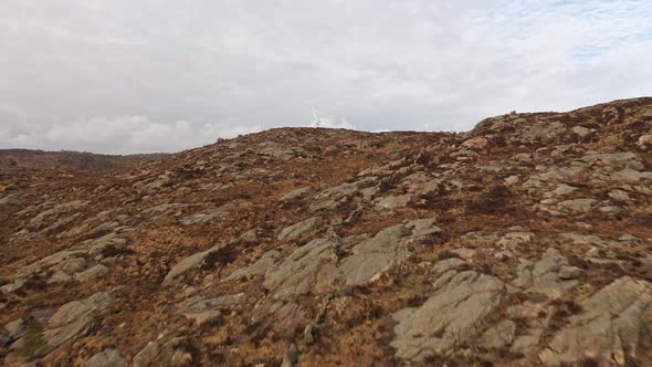 Flying up natural hillside and revealing two wind turbines behind hill at Lindesnes wind park in sou