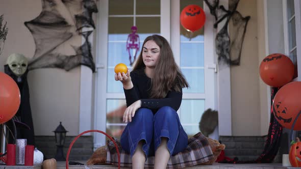 Portrait of Happy Young Beautiful Caucasian Woman Sitting on Backyard Porch on Halloween Smelling