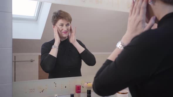 Portrait of Cheerful Caucasian Senior Woman Looking at Her Reflection in Big Mirror, Smiling