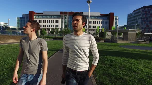 4k back view two young multi ethnic men outdoor walking with smart phone having conversation