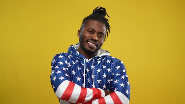 Cheerful African American Young Man in Hoodie with US Flag Print Crossing Hands Posing at Yellow