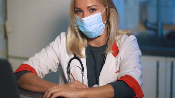 Female Doctor in Surgical Mask Using Laptop Looking at you