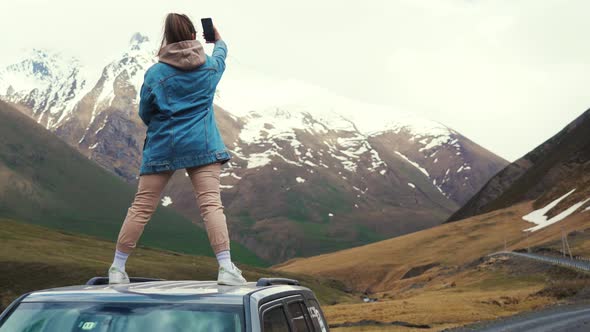 Girl Standing on the Roof of the Car and Taking a Selfie in Kazbegi Mountains Georgia