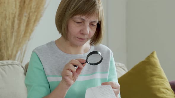Woman Looks at a Receipt From a Supermarket Through a Magnifying Glass
