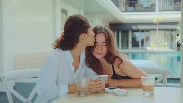 Happy Female Couple Using a Smartphone While Drinking Coffee