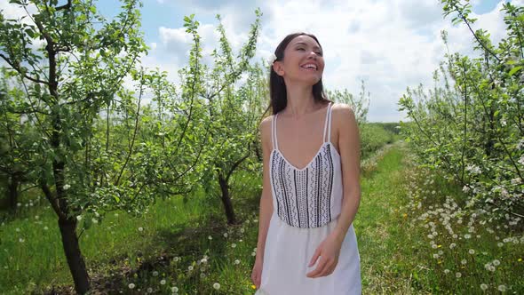 Young Happy Woman Walking Around Blooming Orchard