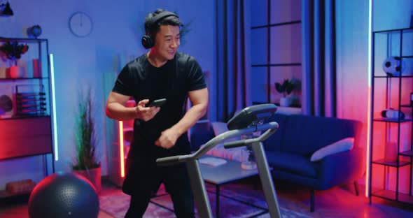 Asian Guy in Training Clothes Enjoying Dancing Music in Earphones While Doing Stepping Exercises