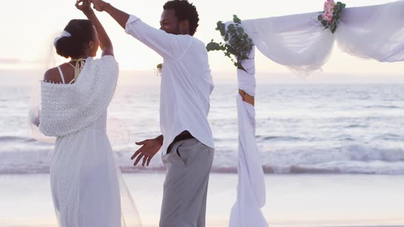 African american couple in love getting married, smiling and dancing on the beach at sunset