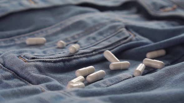 handful of white medical capsules fall on blue jeans. 