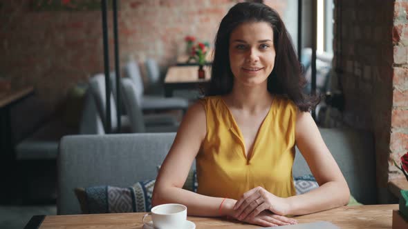 Portrait of Attractive Girl Sitting in Cafe with Drink Looking at Camera Smiling