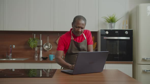 Retired African Male Networking on Laptop in Kitchen