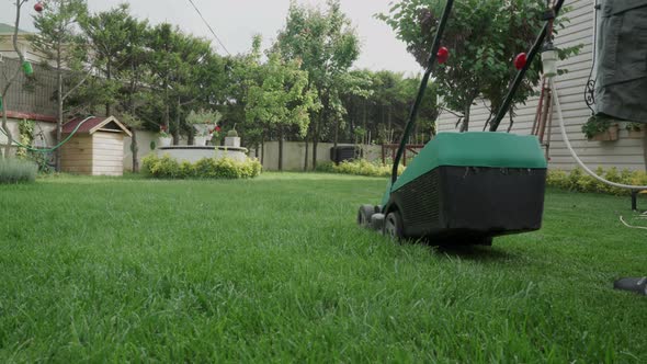 An old man mowing the grasses in his lawn with a electrical lawn mower.