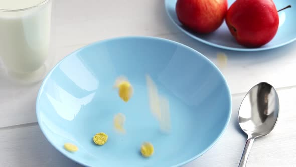 Corn Flakes are Poured Into Blue Bowl on Wooden Table