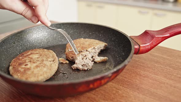 Fish cutlets in a frying pan with oil. Male hand with a fork.