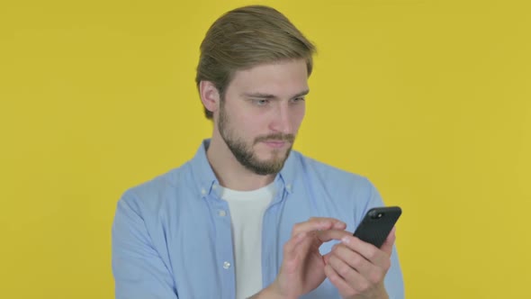 Young Man Browsing Smartphone on Yellow Background