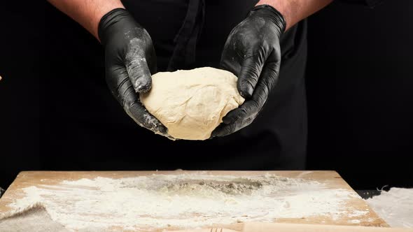 male chef in black uniform and black latex gloves throws kneaded dough 