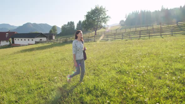 Girl Walking in a Field Near an Alpine Village