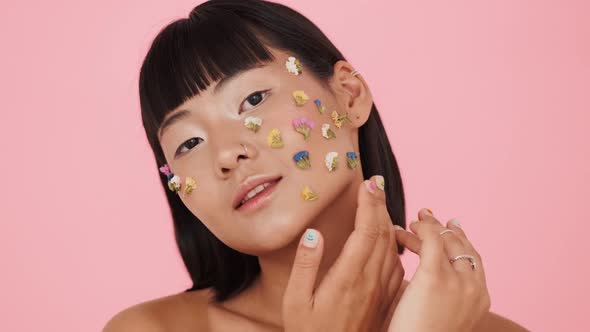 A charming brunette asian woman posing with colorful flowers on her face