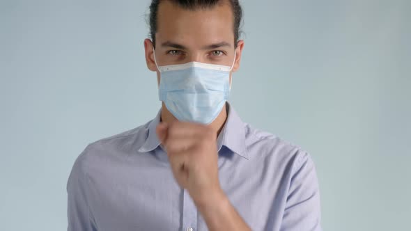 Young man wearing a protective medical face mask coughing from a viral infection.