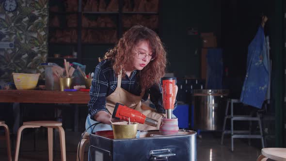 Woman with Curly Hair Heating Up a Fresh New Pot on the Potter's Wheel