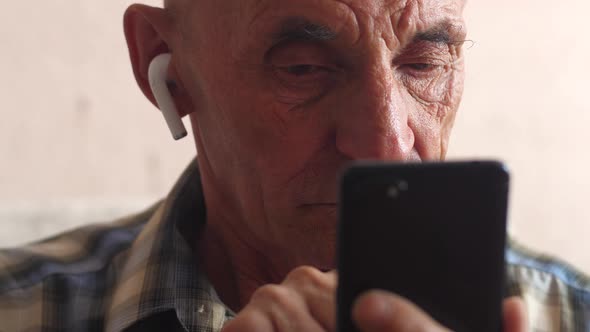 Caucasian pensioner serious 70-79 years old in headphones writes a text by pressing a finger on the 