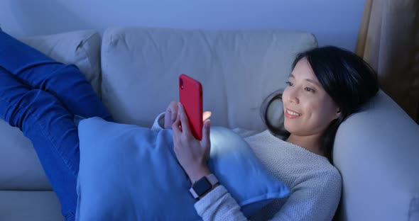 Woman use of mobile phone and lying down on sofa at home in the evening