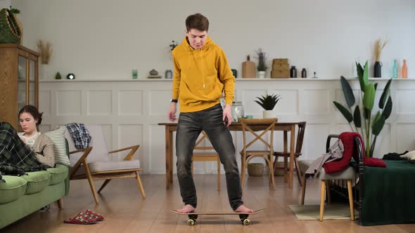 Young funny man at home learning to stand on a skateboard and falls