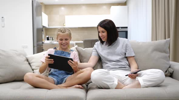 Young Mother and Teen Daughter Resting on the Sofa at Home and Using the Tablet Device and