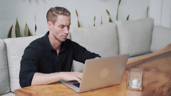 Man Freelancer Sitting at Table Using Laptop for Work in Modern Cafe