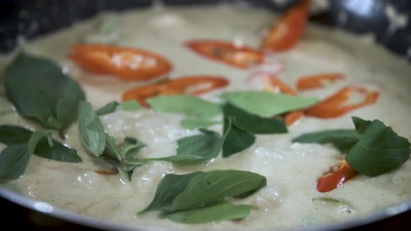 Garnishing Boiling Green Curry with Red Chili and Green Thai Basil - Close Up